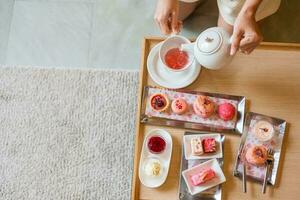 Woman hand pouring hot tea with Afternoon tea set and Pink dessert at luxury hotel photo
