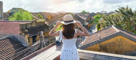 happy traveler traveling at Hoi An ancient town in Vietnam, woman with dress and hat sightseeing view at rooftop.landmark and popular for tourist attractions. Vietnam and Southeast Asia travel concept photo