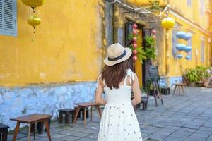 happy traveler sightseeing at Hoi An ancient town in central Vietnam, woman with dress and hat traveling. landmark and popular for tourist attractions. Vietnam and Southeast Asia travel concept photo