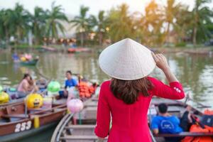 happy woman wearing Ao Dai Vietnamese dress, traveler visit Thu Bon River and Sightseeing Boat Ride at Hoi An ancient town. landmark for tourist attractions.Vietnam and Southeast travel concept photo