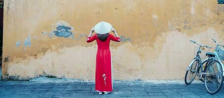 happy woman wearing Ao Dai Vietnamese dress and hat, traveler sightseeing at Hoi An ancient town in central Vietnam. landmark and popular for tourist attractions. Vietnam and Southeast travel concept photo