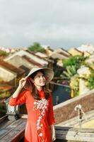 happy woman wearing Ao Dai Vietnamese dress, traveler sightseeing view at rooftop in Hoi An ancient town. landmark and popular for tourist attractions. Vietnam and Southeast travel concept photo