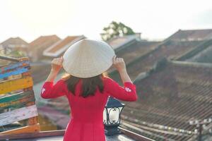 contento mujer vistiendo ao dai vietnamita vestido, viajero Turismo ver a techo en hoi un antiguo ciudad. punto de referencia y popular para turista atracciones Vietnam y Sureste viaje concepto foto