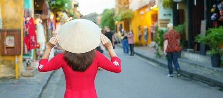 happy woman wearing Ao Dai Vietnamese dress, asian traveler sightseeing at Hoi An ancient town in central Vietnam. landmark and popular for tourist attractions. Vietnam and Southeast travel concept photo