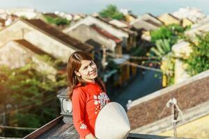 happy woman wearing Ao Dai Vietnamese dress, traveler sightseeing view at rooftop in Hoi An ancient town. landmark and popular for tourist attractions. Vietnam and Southeast travel concept photo