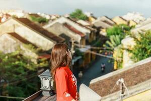 happy woman wearing Ao Dai Vietnamese dress, traveler sightseeing view at rooftop in Hoi An ancient town. landmark and popular for tourist attractions. Vietnam and Southeast travel concept photo