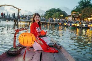woman wearing Ao Dai Vietnamese dress, traveler Sightseeing Boat Ride and floating paper lantern at Hoi An ancient town. landmark for tourist attractions.Vietnam and Southeast travel concept photo