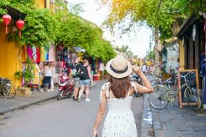 happy traveler sightseeing at Hoi An ancient town in central Vietnam, woman with dress and hat traveling. landmark and popular for tourist attractions. Vietnam and Southeast Asia travel concept photo