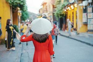 happy woman wearing Ao Dai Vietnamese dress, asian traveler sightseeing at Hoi An ancient town in central Vietnam. landmark and popular for tourist attractions. Vietnam and Southeast travel concept photo