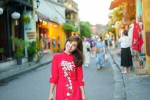 happy woman wearing Ao Dai Vietnamese dress, asian traveler sightseeing at Hoi An ancient town in central Vietnam. landmark and popular for tourist attractions. Vietnam and Southeast travel concept photo