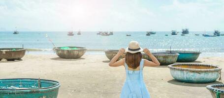 Woman traveler visiting at My Khe beach and sightseeing basket finishing boats. Tourist with blue dress and hat traveling in Da Nang city. Vietnam and Southeast Asia travel concept photo