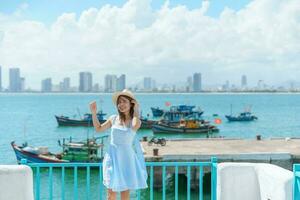 mujer viajero visitando a hijo tra puerto pequeño. turista con azul vestir y sombrero de viaje en da nang ciudad. Vietnam y Sureste Asia viaje concepto foto