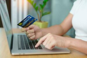 woman hand holding credit card and using laptop for online shopping while making order at home. Marketplace platform website, technology, ecommerce, digital banking and online payment concept photo
