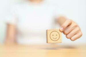 Hand choosing happy face from Emotion block for customer review, good experience, positive feedback, satisfaction, survey, evaluation, assessment, mood and world mental health day concept photo