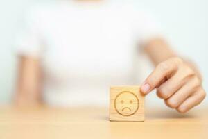 Hand choosing unhappy angry face from Emotion block. customer review, bad experience, negative feedback, satisfaction, survey, rating service, assessment, mood, world mental health day concepts photo
