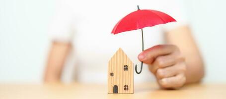 Businesswoman hand holding red Umbrella cover wooden Home model. real estate, insurance and property concepts photo