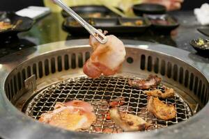 mano interrogatorio intenso carne Cerdo en estufa servir en restaurante. japonés comida y coreano barbacoa tradicional estilo foto