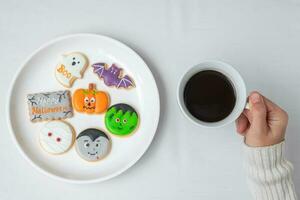 woman hand holding coffee cup during eating funny Halloween Cookies. Happy Halloween day, Trick or Threat, Hello October, fall autumn, Traditional, party and holiday concept photo