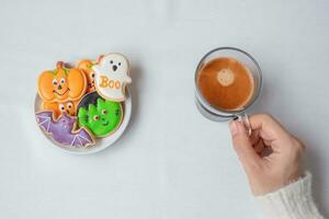 woman hand holding coffee cup during eating funny Halloween Cookies. Happy Halloween day, Trick or Threat, Hello October, fall autumn, Traditional, party and holiday concept photo