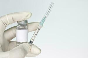 Left hand with medical gloves holding vial and syringe on a whi photo