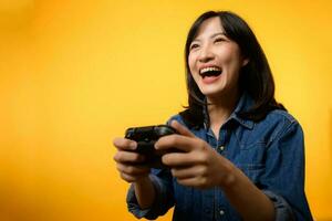 Portrait young asian woman with happy success smile wearing denim clothes holding joystick controller and playing video game. Fun and relax hobby entertainment lifestyle concept. photo