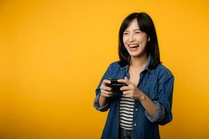 Portrait young asian woman with happy success smile wearing denim clothes holding joystick controller and playing video game. Fun and relax hobby entertainment lifestyle concept. photo