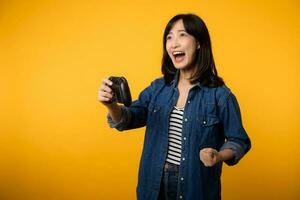 Portrait young asian woman with happy success smile wearing denim clothes holding joystick controller and playing video game. Fun and relax hobby entertainment lifestyle concept. photo