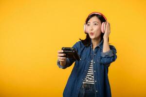 Portrait young asian woman with happy success smile wearing denim clothes holding joystick controller and playing video game. Fun and relax hobby entertainment lifestyle concept. photo