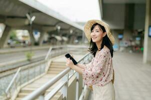 Asian young woman traveler with weaving basket using a mobile phone beside railway train station in Bangkok. Journey trip lifestyle, world travel explorer or Asia summer tourism concept. photo