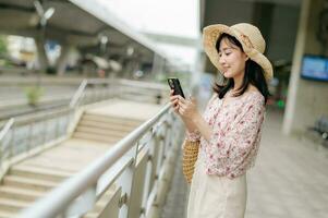 Asian young woman traveler with weaving basket using a mobile phone beside railway train station in Bangkok. Journey trip lifestyle, world travel explorer or Asia summer tourism concept. photo