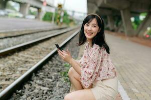 Asian young woman traveler with weaving basket using a mobile phone beside railway train station in Bangkok. Journey trip lifestyle, world travel explorer or Asia summer tourism concept. photo