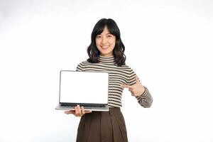 Beautiful young Asian woman on sweater cloth pointing index finger on laptop pc computer and looking at camera with smile face and happy isolated on white background photo