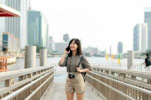 Young Asian woman backpack traveler using mobile phone in express boat pier on Chao Phraya River in Bangkok. photo