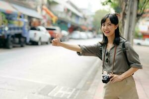 Smiling young Asian woman traveler hitchhiking on a road in the city. Life is a journey concept. photo