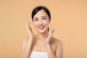 Beautiful girl asian model touching fresh glowing hydrated facial skin on beige background closeup. Beauty face young woman with natural makeup and healthy skin portrait. Skin care concept photo