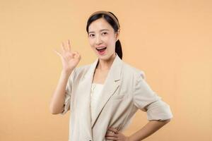 Studio portrait of happy successful confident young asian business woman. Beautiful young lady in white jacket smiling at camera standing isolated on solid beige colour copyspace background photo