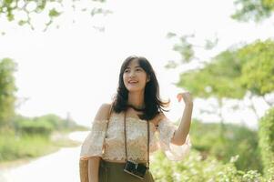 Portrait of asian young woman traveler with weaving hat and basket and a camera on green public park nature background. Journey trip lifestyle, world travel explorer or Asia summer tourism concept. photo