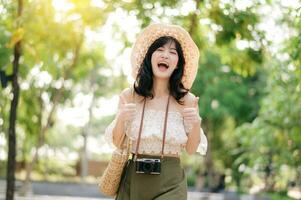 Portrait of asian young woman traveler with weaving hat and basket and a camera on green public park nature background. Journey trip lifestyle, world travel explorer or Asia summer tourism concept. photo