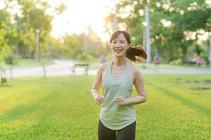 Fit Asian young woman jogging in park smiling happy running and enjoying a healthy outdoor lifestyle. Female jogger. Fitness runner girl in public park. healthy lifestyle and wellness being concept photo