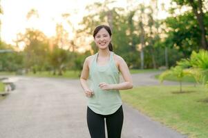 Fit Asian young woman jogging in park smiling happy running and enjoying a healthy outdoor lifestyle. Female jogger. Fitness runner girl in public park. healthy lifestyle and wellness being concept photo