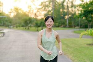 Fit Asian young woman jogging in park smiling happy running and enjoying a healthy outdoor lifestyle. Female jogger. Fitness runner girl in public park. healthy lifestyle and wellness being concept photo