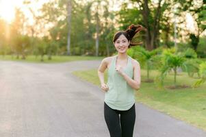 Fit Asian young woman jogging in park smiling happy running and enjoying a healthy outdoor lifestyle. Female jogger. Fitness runner girl in public park. healthy lifestyle and wellness being concept photo