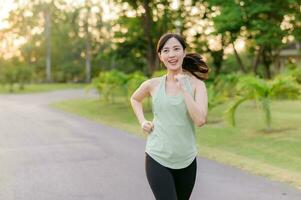 Fit Asian young woman jogging in park smiling happy running and enjoying a healthy outdoor lifestyle. Female jogger. Fitness runner girl in public park. healthy lifestyle and wellness being concept photo