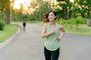 Fit Asian young woman jogging in park smiling happy running and enjoying a healthy outdoor lifestyle. Female jogger. Fitness runner girl in public park. healthy lifestyle and wellness being concept photo