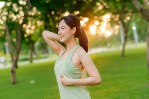 hembra persona que practica jogging. ajuste joven asiático mujer con verde ropa de deporte extensión músculo en parque antes de corriendo y disfrutando un sano exterior. aptitud corredor niña en público parque. bienestar siendo concepto foto