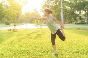 Female jogger. Fit young Asian woman with green sportswear stretching muscle in park before running and enjoying a healthy outdoor. Fitness runner girl in public park. Wellness being concept photo