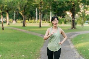 Fit young Asian woman jogging in park smiling happy running and enjoying a healthy outdoor lifestyle. Female jogger. Fitness runner girl in public park. healthy lifestyle and wellness being concept photo