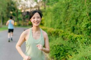 Fit Asian young woman jogging in park smiling happy running and enjoying a healthy outdoor lifestyle. Female jogger. Fitness runner girl in public park. healthy lifestyle and wellness being concept photo