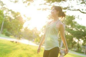 Female jogger. Fit young Asian woman with green sportswear stretching muscle in park before running and enjoying a healthy outdoor. Fitness runner girl in public park. Wellness being concept photo