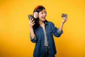 Portrait young asian woman with happy success smile wearing denim clothes and headphone holding smartphone and credit card. Shopping online mobile phone entertainment lifestyle concept. photo